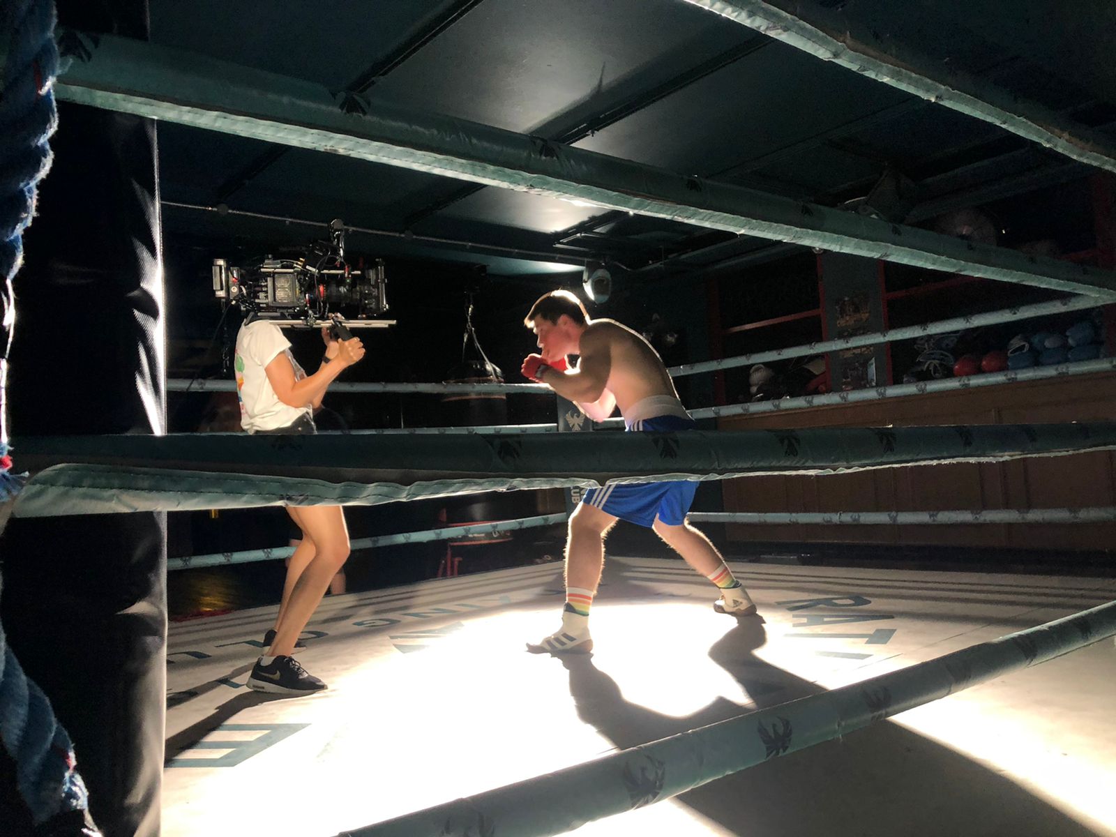 A cameraperson stands in a boxing ring with Jill as Jill stands in a boxing stance facing the camera.