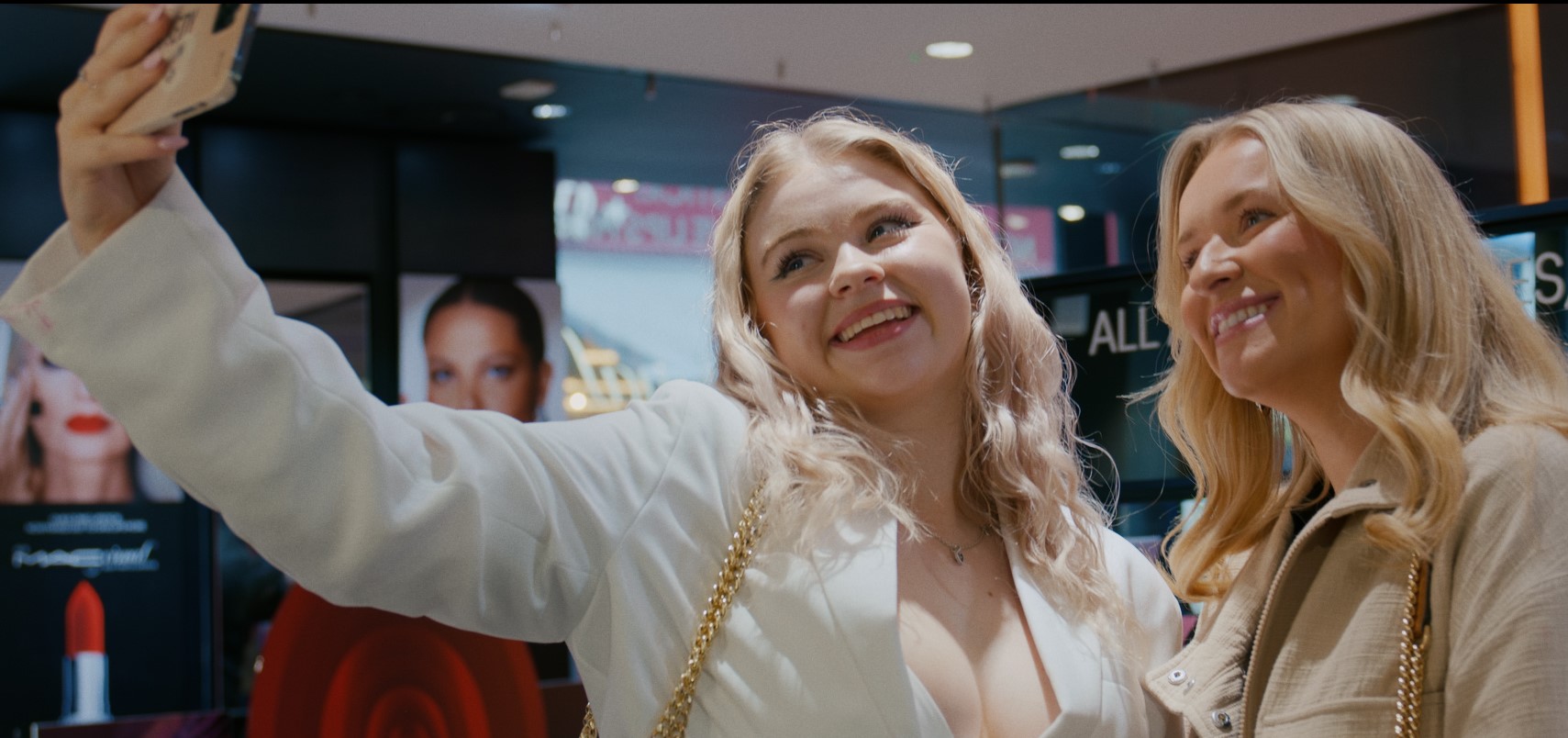 Jazzy Whipps taking a selfie with another blonde haired friend. They are both wearing light coloured blazers and smiling for the camera.