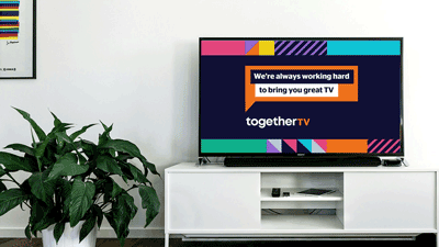 Television placed on a television stand. Text reads: We're always working hard to bring you great TV. There is a house plant next to the television stand. 