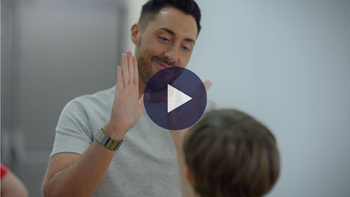 Still from Love, Dad and Daddy. Ross Adams is facing the camera and high-fiving a child who's back is towards us. Ross is smiling